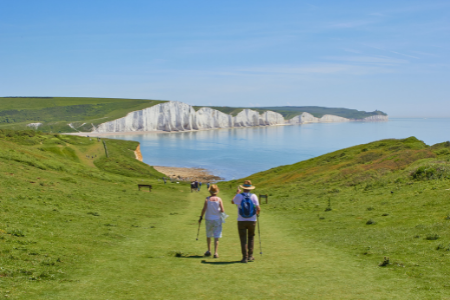 An older couple walking on a grassy path toward the water.